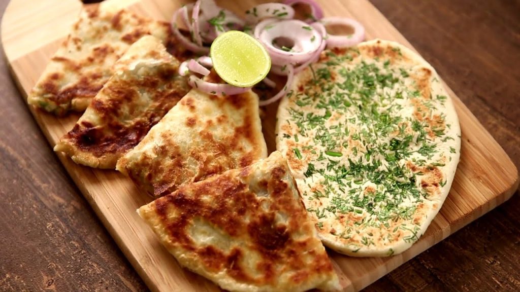 A close-up of golden-brown Amritsari Kulchas fresh out of the tandoor oven, showing their crusty exterior and fluffy interior.