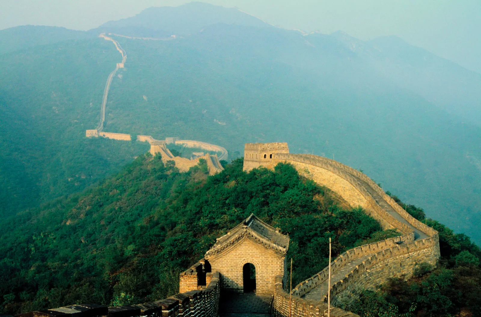 Aerial view of the Great Wall of China winding through mountainous terrain, showcasing its vast length and rugged landscape.